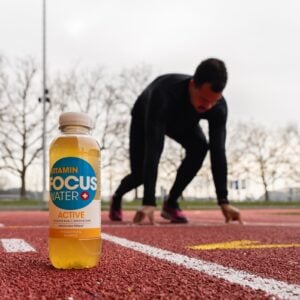 Eine Focuswater Active Vitaminwasser Flasche steht auf dem Boden vor einem Sprinter der sich in Position bringt