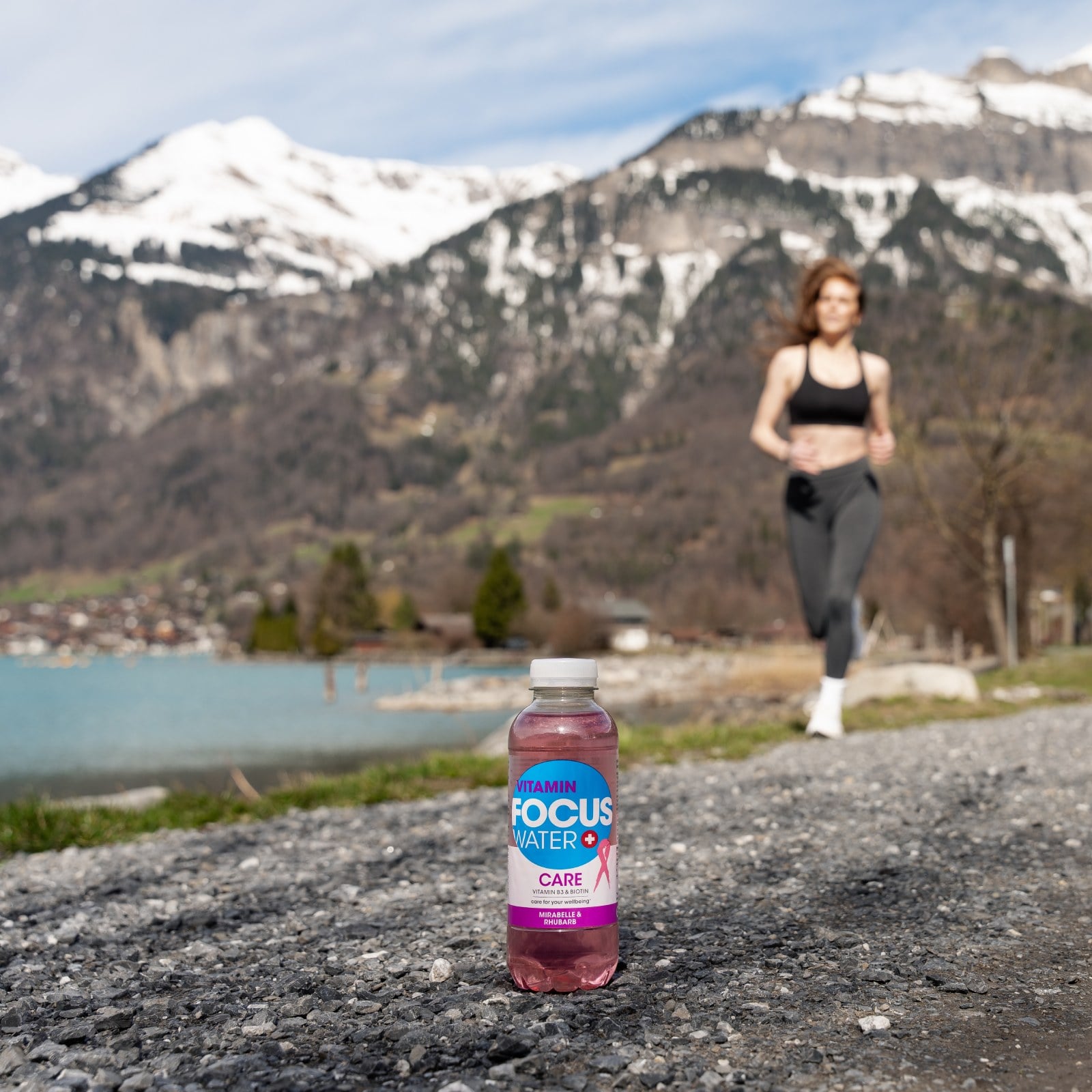 Eine Flasche Focuswater Care Vitaminwasser steht auf einem Weg und im Hintergrund läuft eine junge Frau