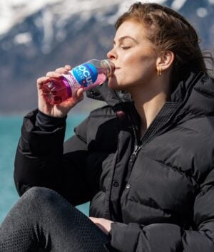 Eine junge Frau trinkt ein Focuswater Care Vitaminwasser an einem See