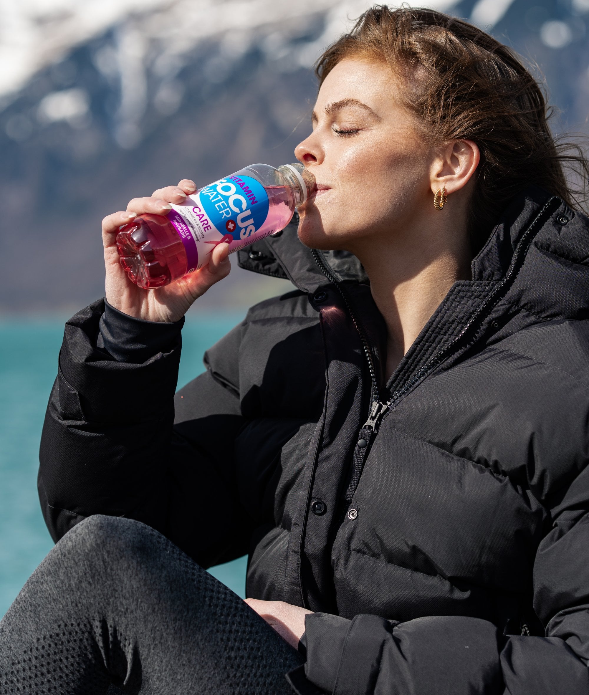 Eine junge Frau trinkt ein Focuswater Care Vitaminwasser an einem See
