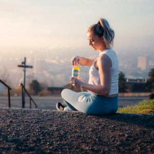 Eine junge Sportlerin sitzt auf einer Treppe und öffnet eine Flasche Focuswater Immunity Vitaminwasser