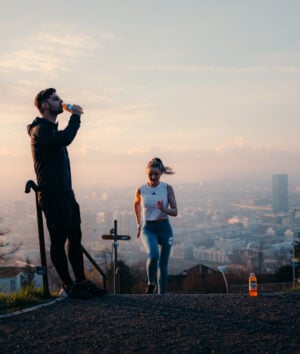 Eine Sportlerin rennt eine Treppe hoch und ihr Trainer trinkt Focuswater Immunity Vitaminwasser