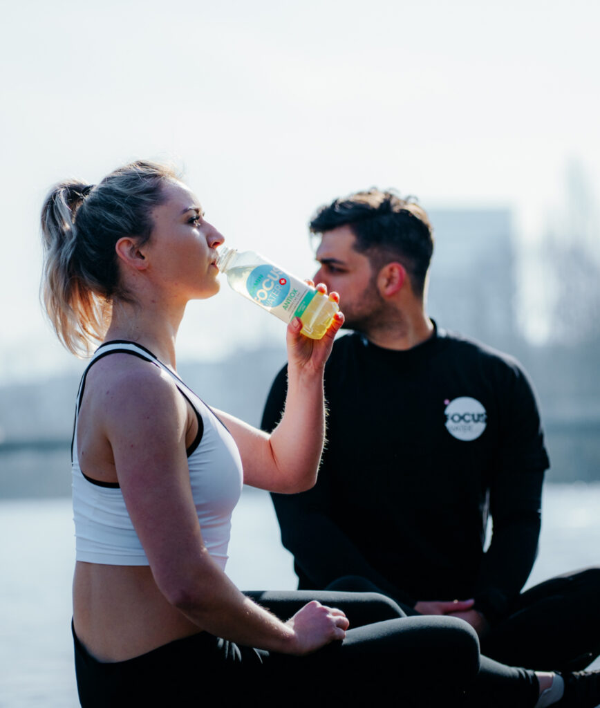 Zwei Sportler trinken sitzend Focuswater Antiox Vitaminwasser