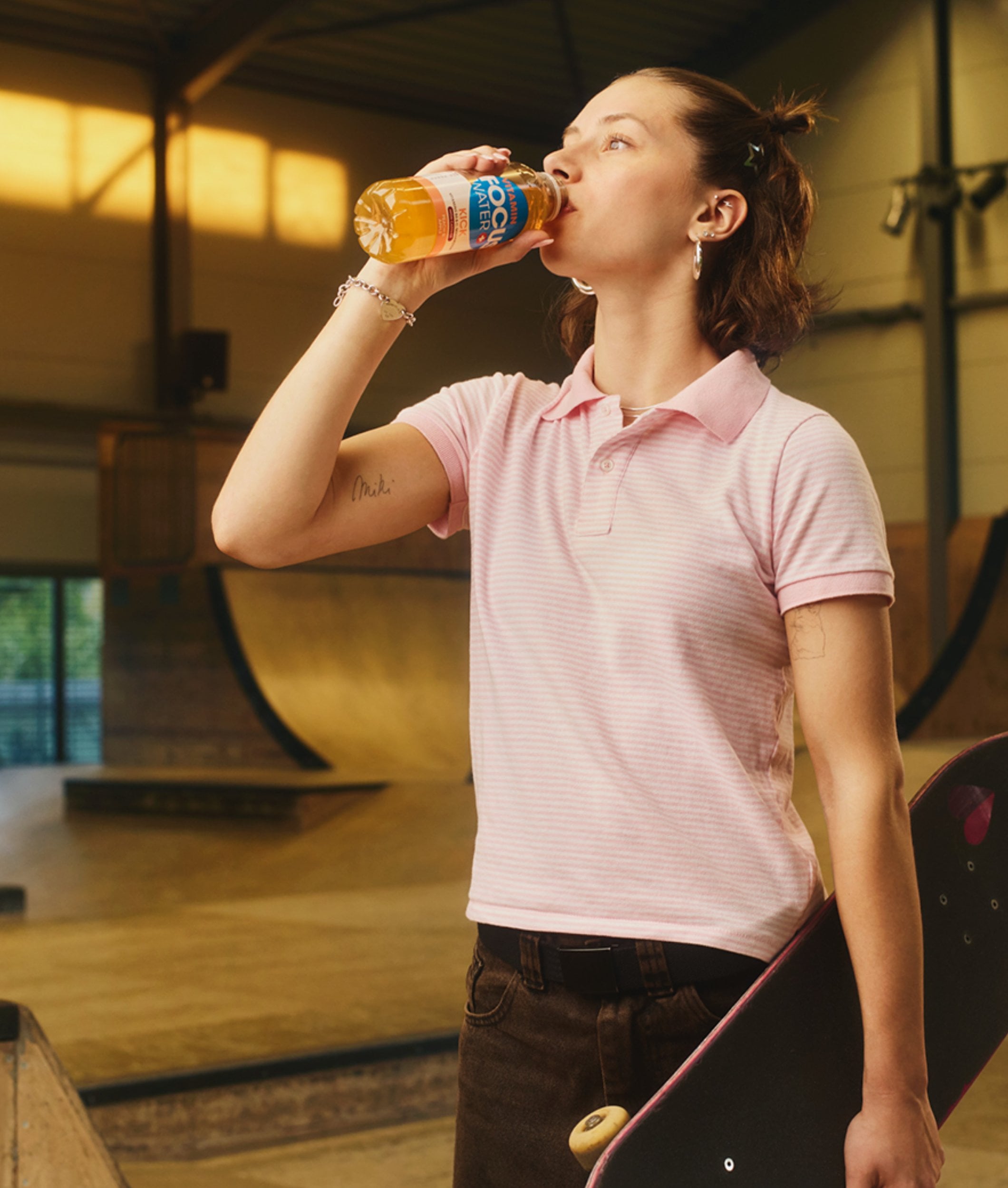 Junge Frau trinkt Focuswater Kick im Skatepark, fruchtig und erfrischend.