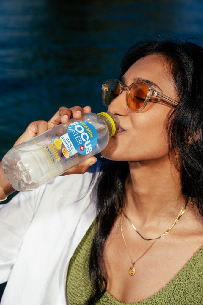 Frau trinkt Focuswater Shine draussen, genießt die Sonne.