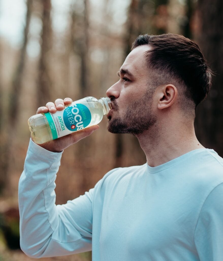Mann trinkt Focuswater Antiox im Wald, entspanntes Outdoor-Erlebnis.