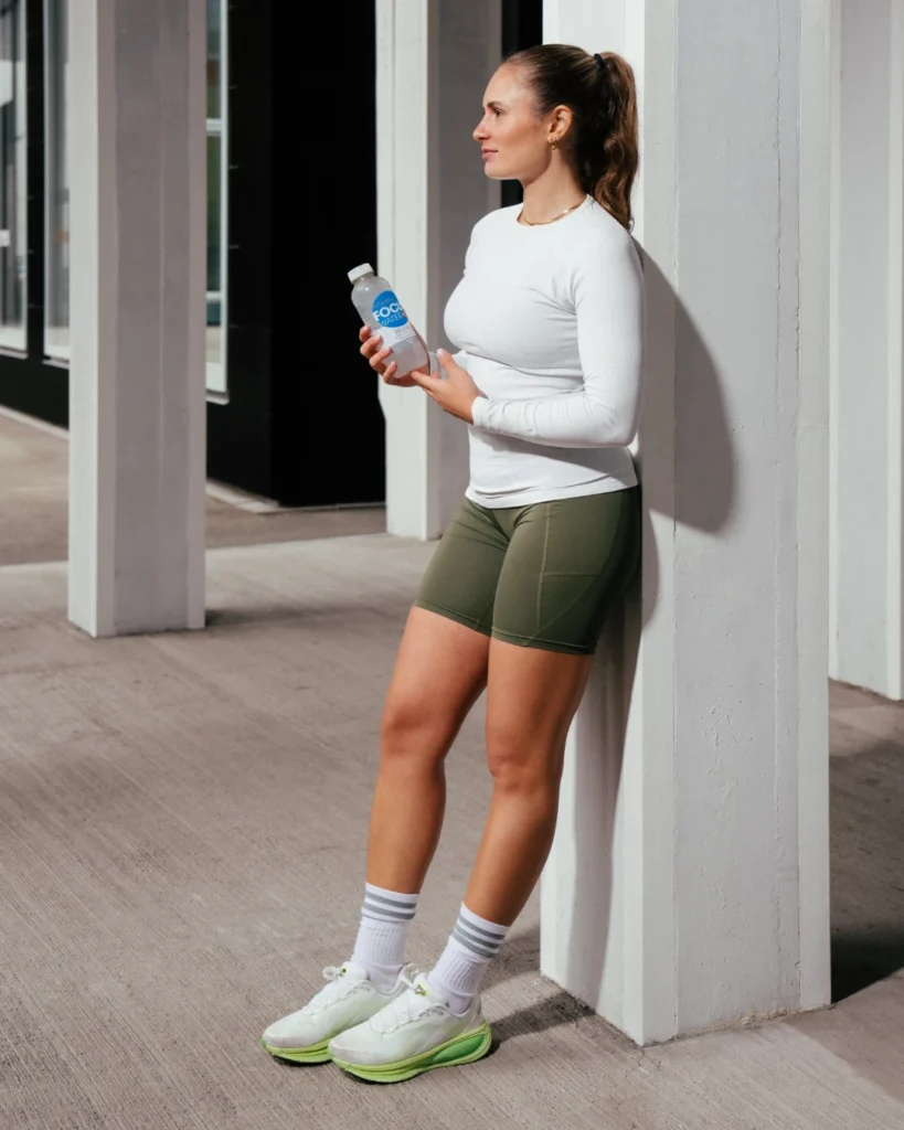 Frau lehnt lächelnd am Pfeiler mit Focuswater Flasche in der Hand.