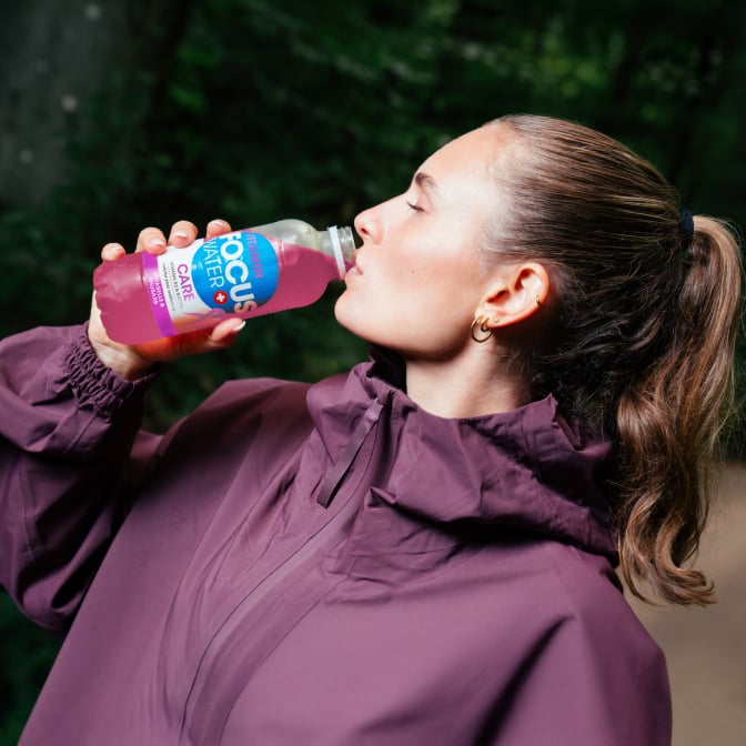 Person trinkt Focuswater Care im Freien, in sportlicher Kleidung.