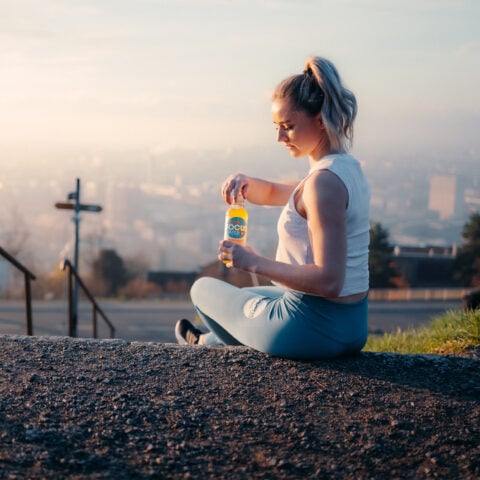 Eine junge Sportlerin sitzt auf einer Treppe und öffnet eine Flasche Focuswater Immunity Vitaminwasser
