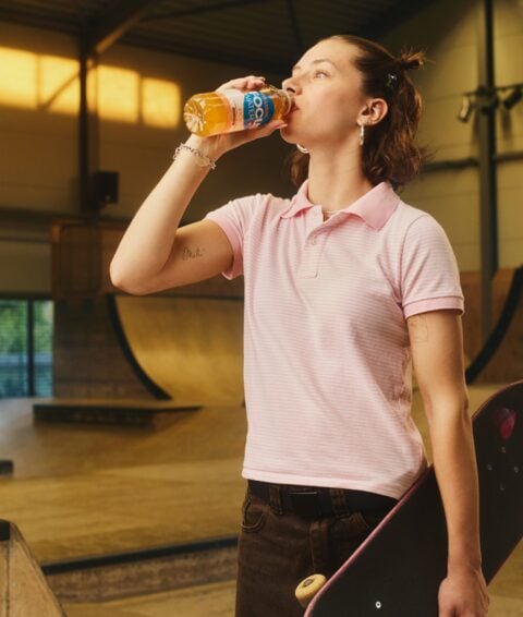 Junge Frau trinkt Focuswater Kick im Skatepark, fruchtig und erfrischend.