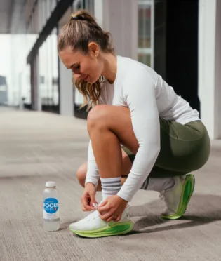 Frau schnürt Schuhe neben Focuswater Reload beim Training.