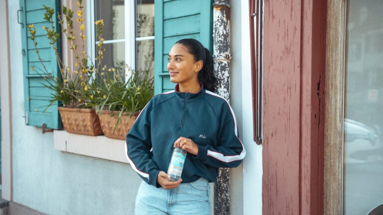 Eine junge Frau steht vor einem Haus mit blauer Wand und hält ein Focuswater Push in der Hand
