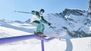 Skifahrer gleitet auf lilafarbener Rail im verschneiten Bergpanorama.