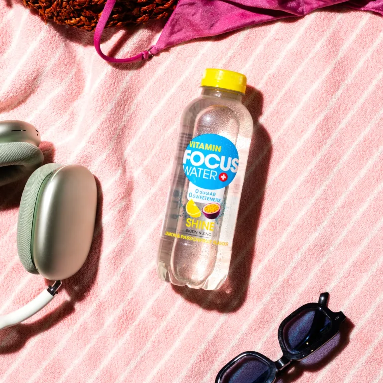 Focuswater Shine Zitrone Passionsfrucht auf gestreiftem Handtuch mit Kopfhörern.