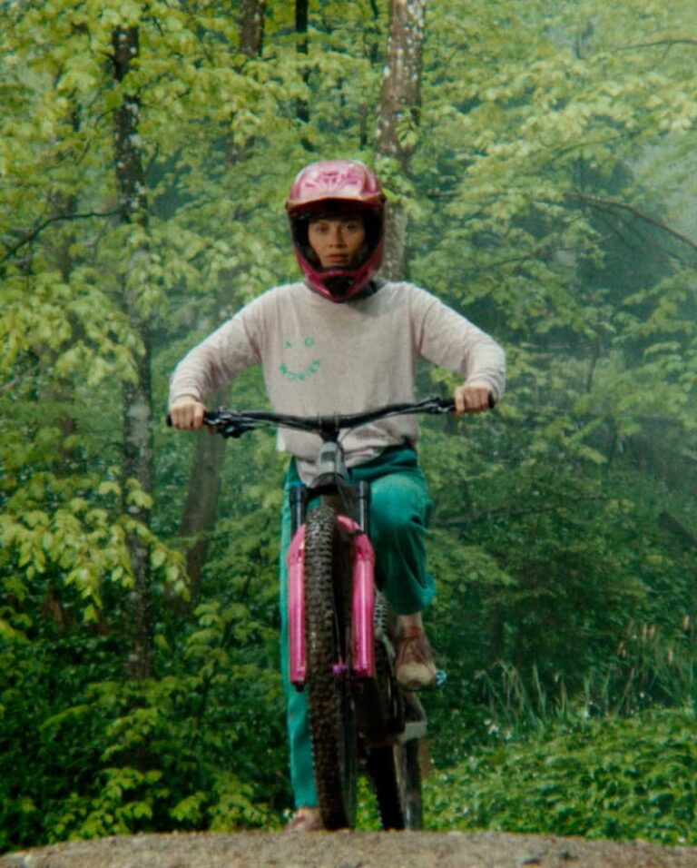 Person fährt Mountainbike durch grünen Wald, trägt pinken Helm.