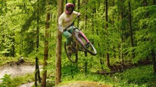 Mountainbikerin springt in grünem Wald.