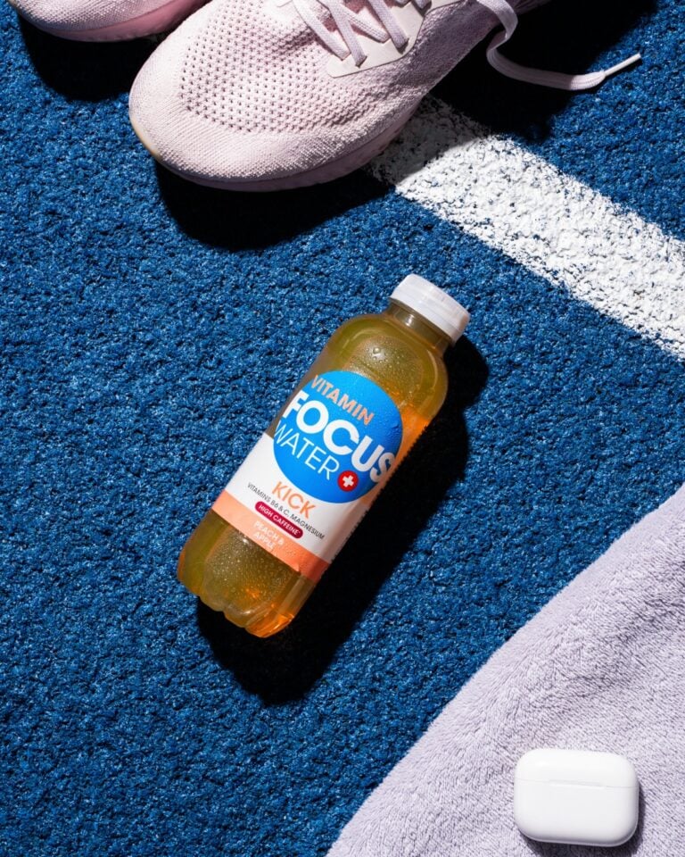 Focuswater Kick Flasche liegt neben Sportschuhen auf blauer Laufbahn.