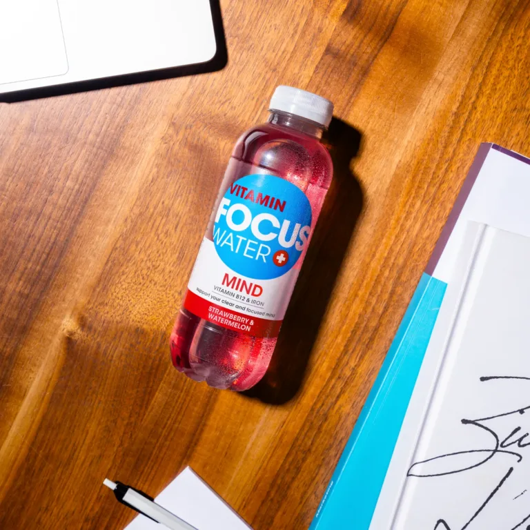 Focuswater Mind Erdbeere Wassermelone auf einem Holztisch neben Notizblock.