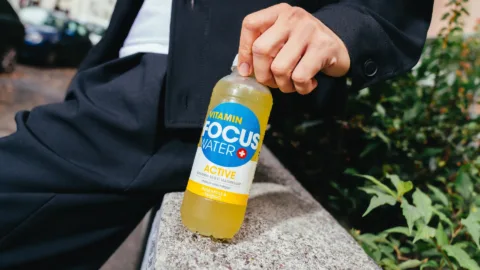 Person hält Focuswater Active Ananas Mango in der Hand, draußen im Freien.