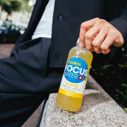 Person hält Focuswater Active Ananas Mango Flasche draußen.
