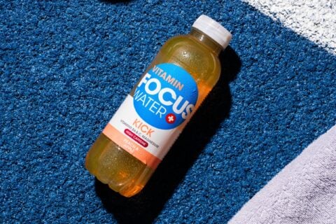 Focuswater Kick Pfirsich Apfel Flasche auf blauer Textur liegend.