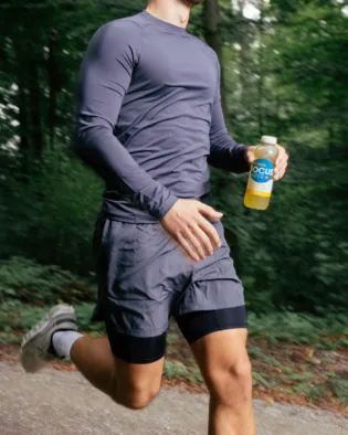 Mann joggt durch einen Wald und hält Focuswater Active Flasche.