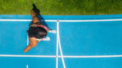 Sportlerin in bunter Kleidung auf blauer Laufbahn vorbereitet.
