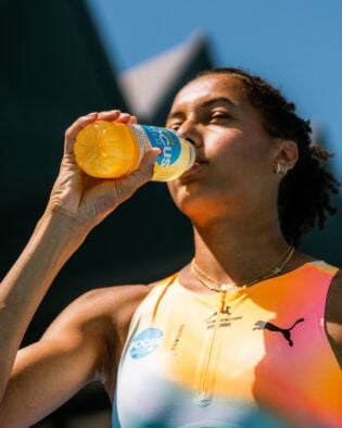 Sportlerin trinkt Focuswater aus Flasche, sonniger Tag im Freien.