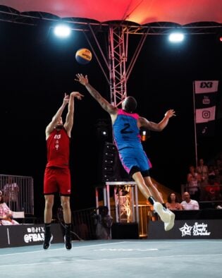 Zwei Basketballspieler im Sprung bei einem nächtlichen Spiel.