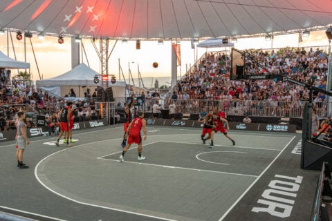 Basketballspiel bei Abenddämmerung vor großem Publikum im Freien.
