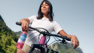 Frau hält Focuswater Flasche auf Fahrrad, Berglandschaft im Hintergrund.